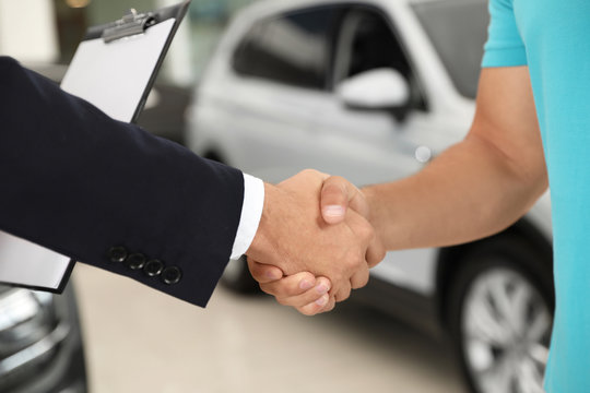 Customer and salesman shaking hands in car salon