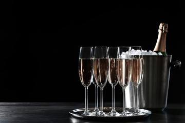 Glasses with champagne and bottle in bucket on dark table