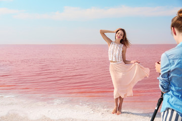 Fototapeta na wymiar Female photographer taking pictures of model near pink lake