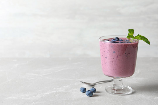 Glass with blueberry smoothie on grey table. Space for text