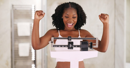 Beautiful black woman happily weighs herself on scale in bathroom