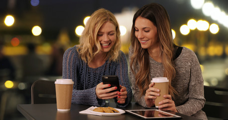 Couple of happy girls drinking using cellphone in Paris, France