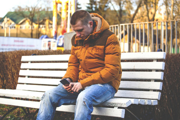 young handsome guy on a bench with a smartphone, retro toned