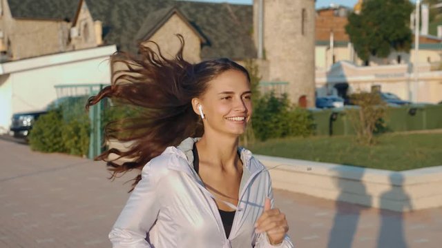 Running woman in park in summer training student run running. Girl sport fitness model in sporty running clothes with bluetooth headphones ear white hands free fit listening music phone earphones
