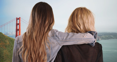 Couple of Caucasian girls holding each other enjoying view of Golden Gate Bridge