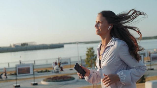 Running woman jogging on beach listening to music in earphones from smart phone bluetooth headphones, Female runner training for marathon on beautiful beach. Mixed race woman.