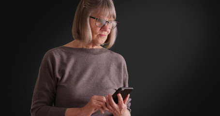 Somber lady reading worrying message on mobile device on dark gray background
