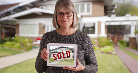 Senior Caucasian female holding tablet with picture of recently sold home 