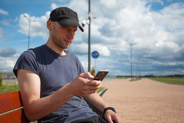 young cute man with a bristle on an outdoor bench with a smartphone