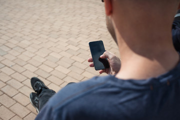 young cute man with a bristle on an outdoor bench with a smartphone