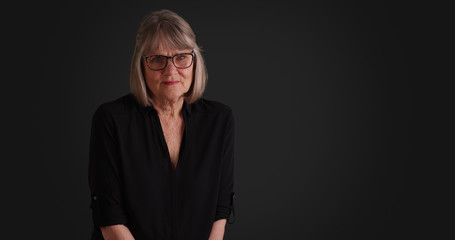 Older woman wearing black outfit looking at camera on solid grey backdrop