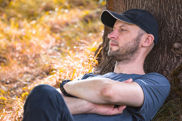 close-up portrait of a brutal man resting in an autumn forest in the shade of a tree