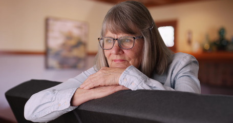 Pensive senior lady resting head on hands and thinking to herself in living room