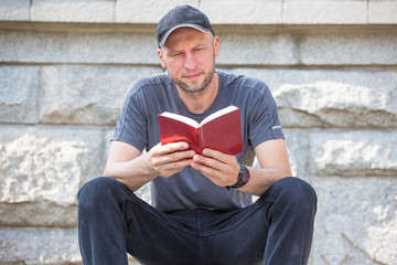 brutal man with a bristles reading a book sitting on a bench outdoors