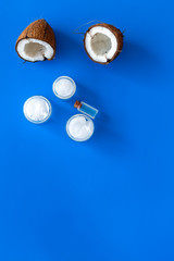 Coconut oil cosmetics for skin and hair care. Oil in small bottle, cream jar, halfs of coconut with shelf on blue background top view copy space