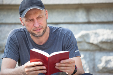 Fototapeta premium brutal man with a bristles reading a book sitting on a bench outdoors