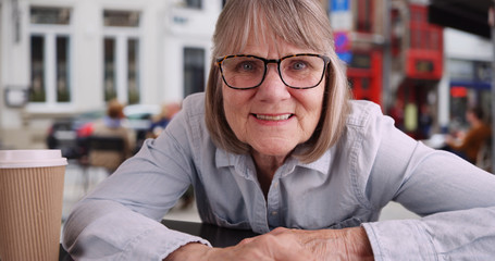 Close up of senior woman smiling to camera outside cafe in European city