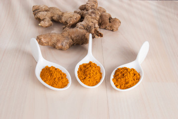 Turmeric powder and fresh turmeric on wooden background.