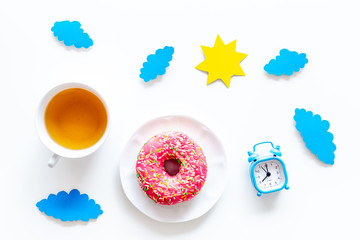 Time for breakfast concept. Tea, donut near alarm clock, sun and clouds cutout on white background top view