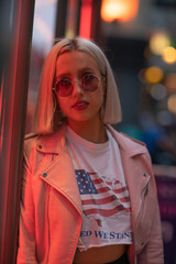 Blond girl in fashionable sunglasses and leather jacket with neon lights