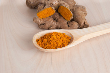 Turmeric powder and fresh turmeric on wooden background.