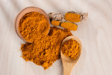 Turmeric powder and fresh turmeric on wooden background.