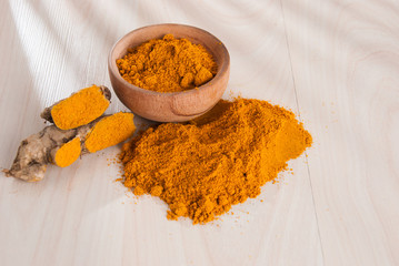 Turmeric powder and fresh turmeric on wooden background.