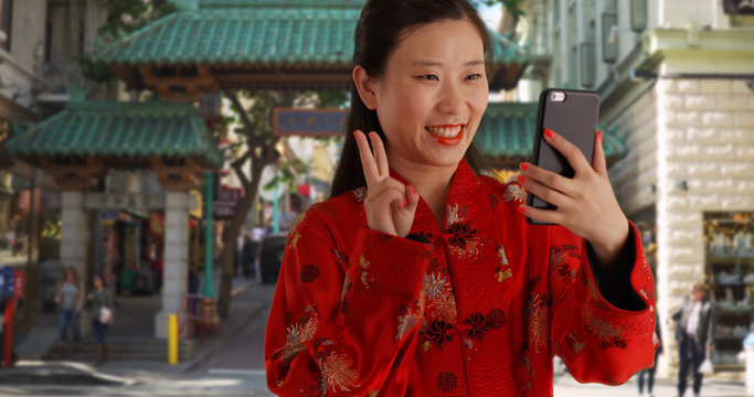 Happy millennial woman taking selfie with smartphone in front of China Town gate