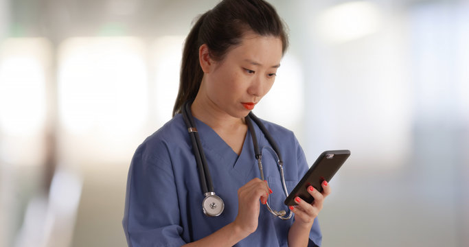 Serious millennial doctor on break reading texts with smartphone inside hospital