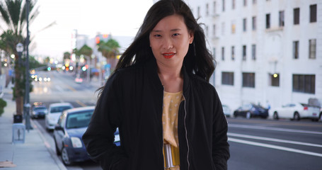 Young Chinese woman in black bomber jacket on city street with hands in pockets
