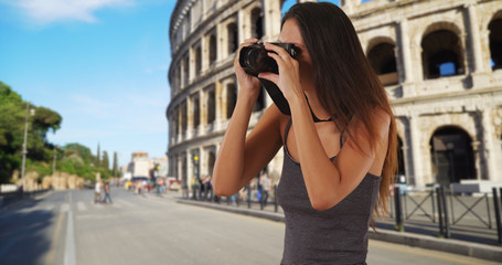 Young tourist woman standing near the Roman Coliseum taking picture with camera