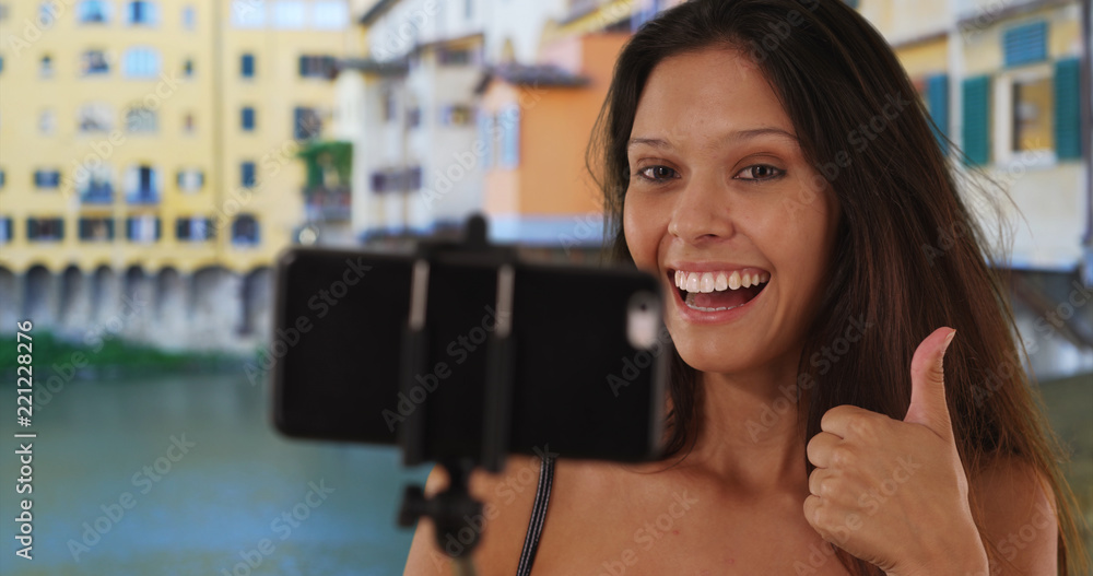 Wall mural Gorgeous young traveler girl using selfie stick near Ponte Vecchio Bridge