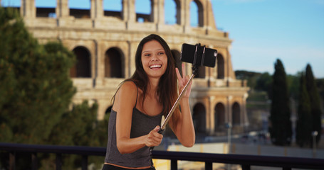 Fototapeta na wymiar Cute brunette traveler girl in front of the Roman Coliseum using selfie stick