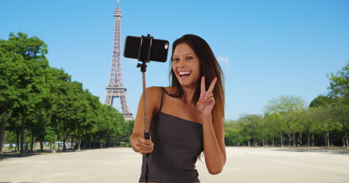 Pretty tourist woman near the Eiffel Tower taking silly photos with selfie stick