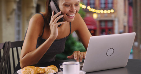 Cheerful young woman talking on mobile phone and working on laptop