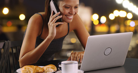 Young woman talking on mobile phone and working on laptop outside at night
