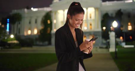 Young female professional texts using cell phone while smiling at night