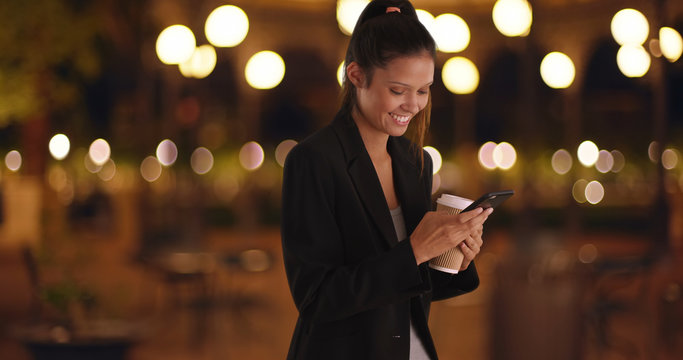 Business woman in black blazer text messaging and smiling at night