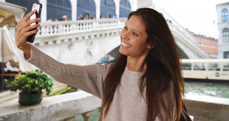 Beautiful female with backpack taking selfie by Grand Canal near Rialto Bridge