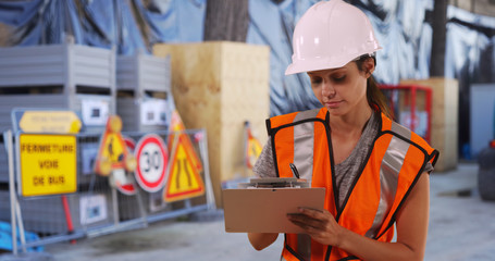 Construction worker in hardhat and safety vest writing on clipboard at work site