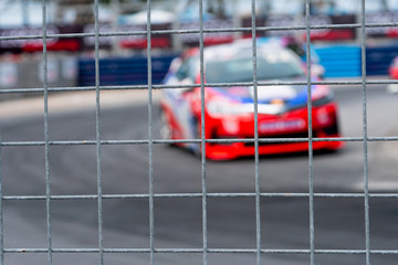 Motorsport car racing on asphalt road. View from the fence mesh netting on blurred car on racetrack background. Super racing car on street circuit. Automotive industry concept.