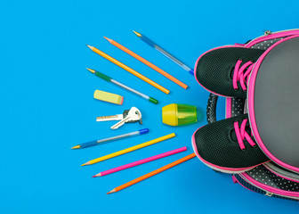 Backpack with sneakers and scattered school accessories and house keys on a blue table. Flat lay.