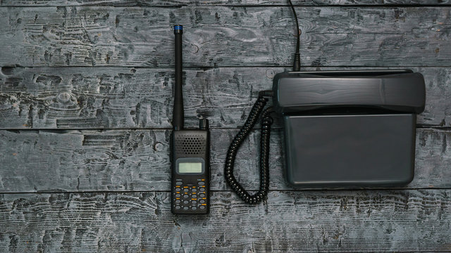 Black and white image of a walkie-talkie and telephone on a wooden table.