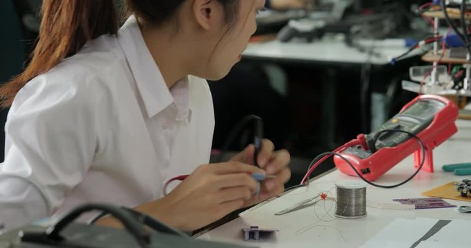 Woman electronics engineer is measuring the signal in the electrical circuit in her workshop. Girl student are studying electronics in classroom.