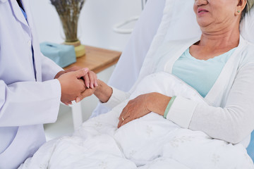 Female doctor holding hand of senior patient to support her