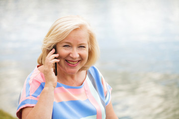 Old Blonde woman calling by phone in summer park