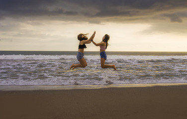 Fototapeta na wymiar back portrait of two happy and attractive young women girlfriends holding hands on the beach running to the sea under beautiful sunset light enjoying summer holidays