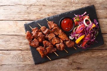 Recipe of a spicy African suya kebab on skewers with fresh vegetable salad and ketchup close-up. Horizontal top view