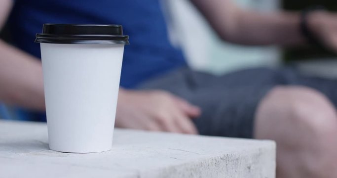 Man sits down in chair with plain white to-go coffee cup in foreground