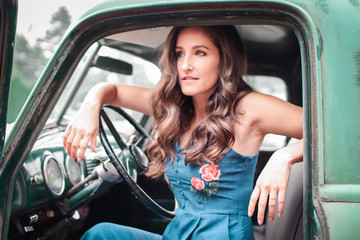 A  beautiful young woman sitting in an old classic pickup truck
